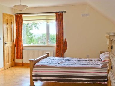 A bedroom with a wooden bed and striped bedding near a window with orange curtains at Sallywood House in Carn near Ballybofey County Donegal