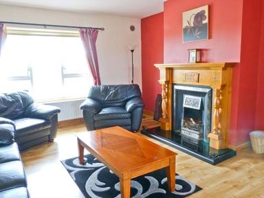 A living room with black leather sofas a wooden coffee table a fireplace with a wooden mantel and a red accent wall at Sallywood House Carn near Ballybofey County Donegal