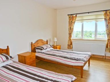 A bedroom with two single beds a wooden nightstand and a window with curtains at Sallywood House Carn near Ballybofey County Donegal