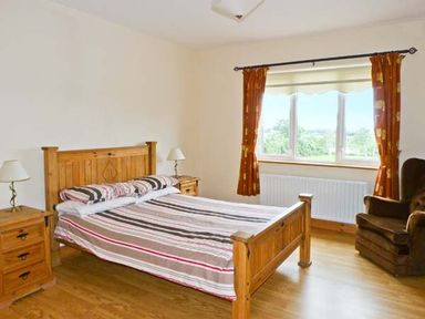 A bedroom with a wooden bed and matching bedside tables with lamps a window with orange curtains and a brown armchair at Sallywood House in Carn near Ballybofey County Donegal