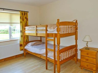 A bedroom with wooden bunk beds, a wooden nightstand with a lamp, and a window with yellow curtains at Sallywood House in Carn near Ballybofey County Donegal