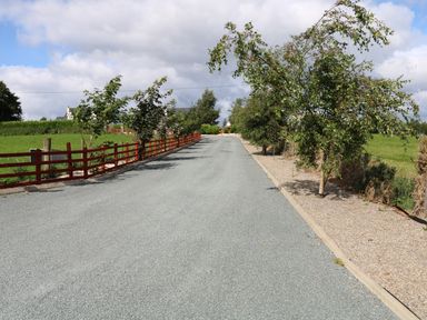 A gravel driveway lined with trees and a red wooden fence with houses visible in the distance at Sallywood House Carn near Ballybofey County Donegal