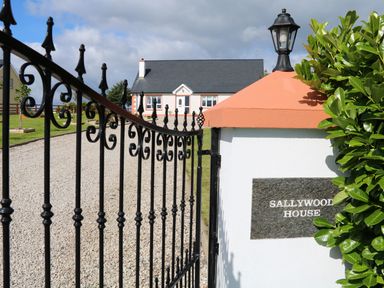 A black metal gate open to a gravel driveway leading to a white house with a dark roof at Sallywood House Carn near Ballybofey County Donegal