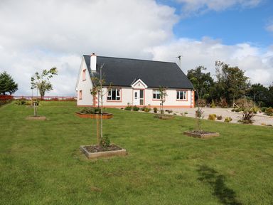 A white house with a black roof surrounded by a lawn with small trees at Sallywood House Carn near Ballybofey County Donegal
