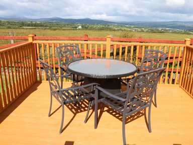 A wooden deck with a round glass table and four metal chairs overlooking a rural landscape at Sallywood House in Carn near Ballybofey County Donegal