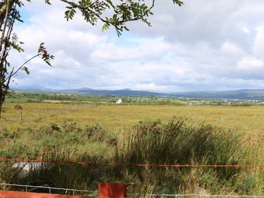 A rural landscape with grass fields bushes a wire fence and distant hills under a cloudy sky at Sallywood House in Carn near Ballybofey County Donegal
