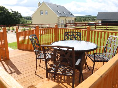A wooden deck with a round glass table and four metal chairs with leaf designs at Sallywood House in Carn near Ballybofey County Donegal
