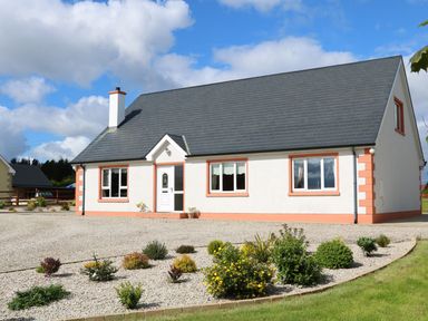 A single story house with gray roof and white walls surrounded by a gravel driveway and small garden at Sallywood House Carn near Ballybofey County Donegal