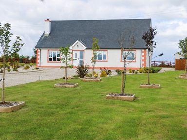 A house with a slate roof and white walls with orange trim in front of a lawn with small trees in square wooden planters at Sallywood House in Carn near Ballybofey County Donegal