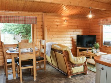 A wooden dining table with chairs and a leather sofa facing a television in a wooden room at Cornfield in Northallerton