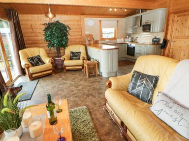 A living room with yellow armchairs a sofa a coffee table with wine glasses and candles and a kitchen area at Cornfield in Northallerton