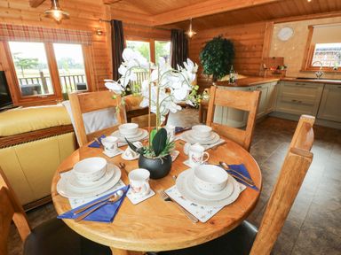 A dining table set with plates bowls mugs and cutlery in a wooden room with kitchen cabinets and large windows at Cornfield in Northallerton