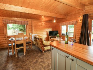 A wooden living room with a dining table, chairs, sofa, television, and a countertop with a bottle and glasses at Cornfield in Northallerton