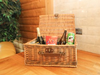 A wicker basket on a wooden table with bottles and a Pringles can in a room with wooden walls and a plant in the corner at Cornfield in Northallerton