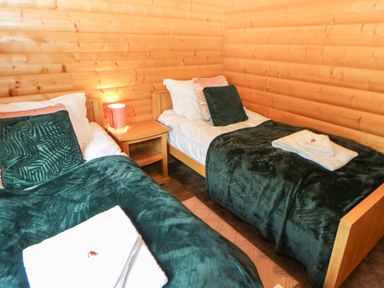 A bedroom with two single beds green blankets wooden walls and a wooden nightstand with a lamp at Cornfield in Northallerton
