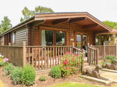 A wooden lodge with a fenced porch and garden with flowers and two dog statues at Cornfield in Northallerton