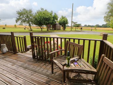 A wooden deck with a table and chairs and a bottle with glasses on the table at Cornfield in Northallerton