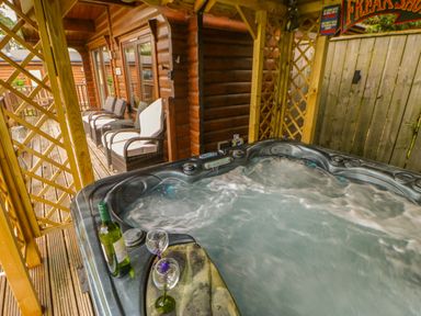An outdoor covered hot tub with a bottle and two glasses on the edge near wooden chairs on a deck at Cornfield in Northallerton