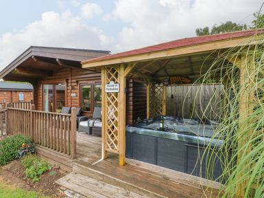 A wooden cabin with outdoor seating and a covered hot tub on a wooden deck at Cornfield in Northallerton