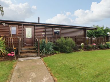 A wooden cabin with a small porch and steps surrounded by plants and grass at Cornfield in Northallerton