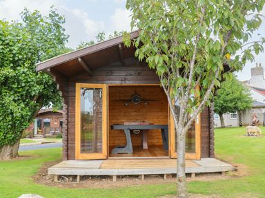 A wooden garden shed with open double doors revealing a foosball table and a clock inside at Cornfield in Northallerton
