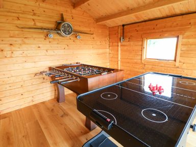 A wooden game room with a foosball table an air hockey table and a wall clock shaped like an airplane at Cornfield in Northallerton