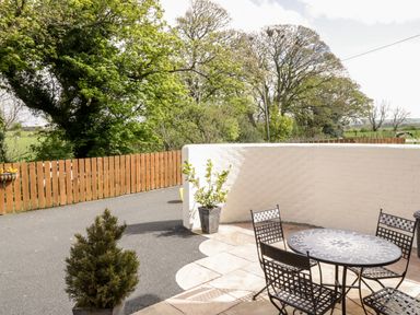 An outdoor patio with a mosaic table and four metal chairs near a white brick wall and wooden fence at The Old Bothy Bolton Low Houses near Wigton