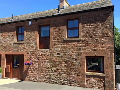 Exterior view of a stone house with three windows one wooden door and a hanging flower basket at The Old Bothy in Bolton Low Houses near Wigton