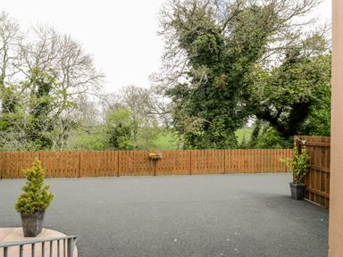 An outdoor paved area with a wooden fence and potted plants near trees at The Old Grainstore in Bolton Low Houses near Wigton