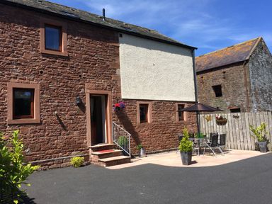 A stone house with a small patio and outdoor table with umbrella at The Old Grainstore in Bolton Low Houses near Wigton
