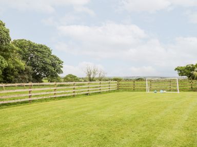 A grassy backyard with a wooden fence trees in the background and a small soccer goal with balls at The Old Grainstore in Bolton Low Houses near Wigton