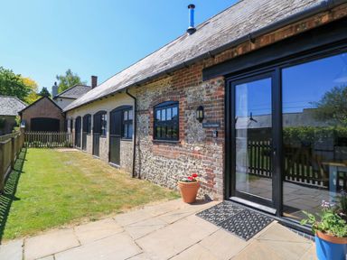 Exterior of a stone and brick building with black doors and windows a small lawn and potted plants at The Old Stables in Winterborne Stickland