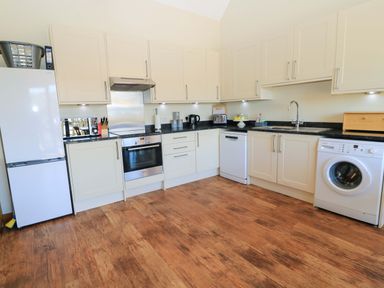A kitchen with white cabinets wooden floor and various appliances at The Old Stables in Winterborne Stickland