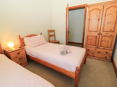 A bedroom with two single beds a wooden wardrobe a wooden chair and a bedside table with a lamp at The Old Stables in Winterborne Stickland