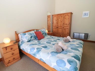 A bedroom with a double bed a wooden wardrobe bedside tables and folded towels on the bed at The Old Stables in Winterborne Stickland