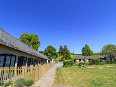 A courtyard with lawns picnic table and cottages with picket fences at The Old Stables in Winterborne Stickland