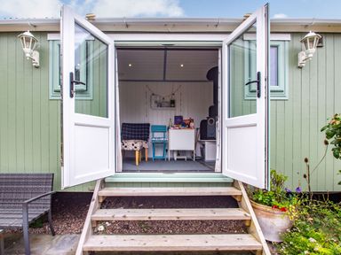 A small porch with open double doors showing a room with chairs and a stove at The Shepherd's Hut in Aberdovey