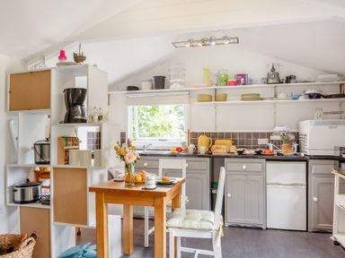 A kitchen with gray cabinets a wooden table with chairs and various kitchen appliances at The Shepherd's Hut in Aberdovey