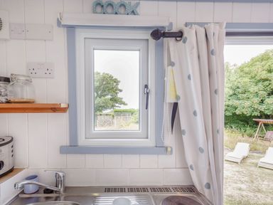 A kitchen window with a sink below and a curtain to the right overlooking a garden at The Shepherd's Hut in Aberdovey