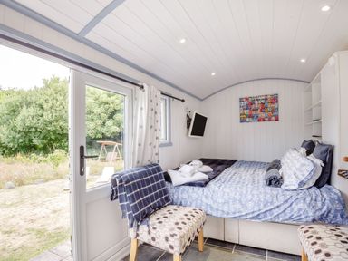 A small bedroom with a bed and patterned chairs next to a glass door showing an outdoor area at The Shepherd's Hut in Aberdovey