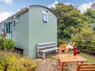A garden with a green hut wooden bench wooden table with flowers wine and two glasses at The Shepherd's Hut in Aberdovey