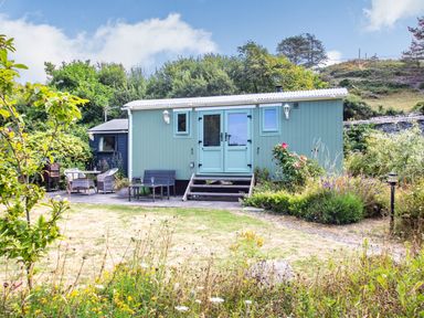 A small building with blue double doors and outdoor seating in a garden at The Shepherd's Hut in Aberdovey