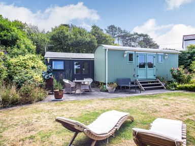 A garden area with two wooden lounge chairs, a patio table with chairs, and two small buildings at The Shepherd's Hut in Aberdovey