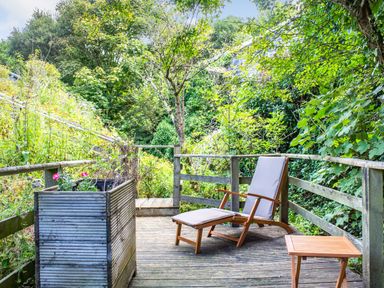 An outdoor wooden deck with a cushioned wooden lounge chair a small wooden table and a planter with plants at The Shepherd's Hut in Aberdovey