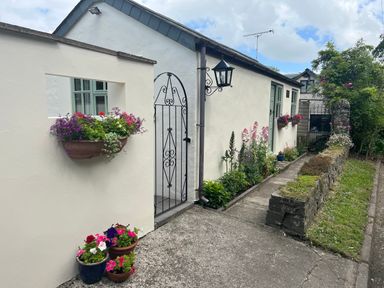 A walkway with flower pots on the ground and flowers in wall-mounted planters outside a white house at Palmers Lodge in Egloskerry near Launceston