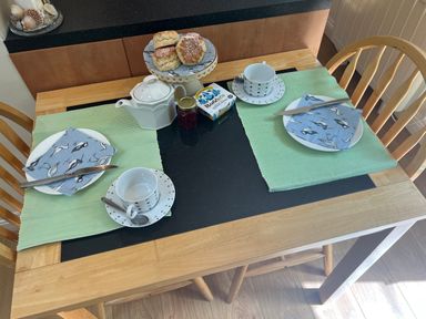 A kitchen table set for two with cups saucers knives napkins scones a teapot clotted cream and jam at Palmers Lodge in Egloskerry near Launceston