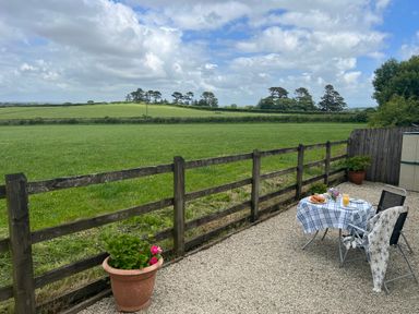 A patio with a small table covered with a checkered cloth two chairs and a view of a grassy field at Palmers Lodge in Egloskerry near Launceston