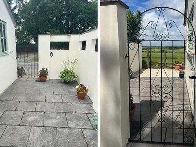 A paved courtyard with white walls and potted plants beside a black wrought iron gate opening to a countryside view at Palmers Lodge Egloskerry near Launceston