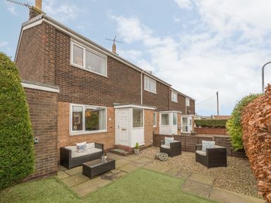 A garden patio with outdoor seating and a brick house with white doors and windows at Crumstone Corner in Seahouses