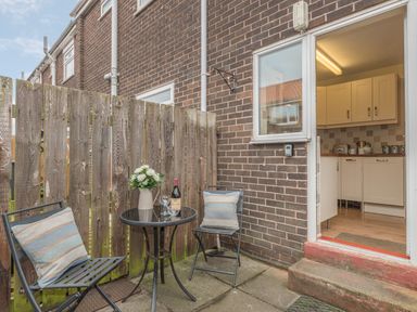 An outdoor patio area with two chairs and a small round table with flowers and a bottle at Crumstone Corner in Seahouses